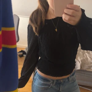 Svart blus med struktur - Säljer en svart blus med strukturmönster. Toppen är croppad med smockad midja och ärmar. Perfekt för dig som gillar trendiga detaljer och en snygg siluett. Passar till vardags men även festligheter