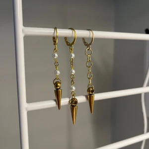 Guldiga örhängen med pärlor och spikes - Unika örhängen i guldton med kedjor, vita pärlor och coola konformade spikes. Perfekt accessoar för dig som vill sticka ut med en edgy men ändå elegant stil. I rostfritt rostfritt stål och handgjort 
