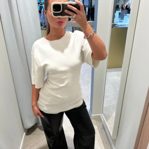 Vit ribbad topp med kort ärm - Säljer en stilren vit topp med ribbad struktur och rund hals. Modellen har korta ärmar och en rak passform som sitter snyggt på kroppen. Perfekt att matcha med både jeans och kostymbyxor. Enkel och clean look.