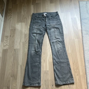Grå bootcut jeans från Gina Tricot - Grå jeans från Gina Tricot med bootcut passform och stora fickor fram och bak. Snygga söm-detaljer längs benen och klassisk knappgylf. 
