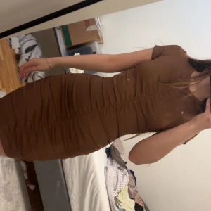 Brun tight kortklänning - Säljer en brun, tight och figurnära kortklänning med korta ärmar. Klänningen har en enkel design med lätt rynkade detaljer längs sidorna och är tillverkad i ett stretchigt material som sitter snyggt på kroppen.