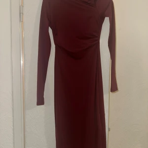 Vinröd långklänning med öppen rygg - Säljer en vinröd långklänning med lång ärm och snyggt öppen rygg. Klänningen har en figurnära passform och är tillverkad i ett mjukt, stretchigt material som sitter skönt på kroppen. Perfekt för dig som vill sticka ut med en elegant och stilren look.
