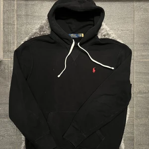 Ralph Lauren Hoodie Svart  - Klassisk svart hoodie från Ralph Lauren. Stilren design med hög komfort, perfekt till vardags och ett tidlöst basplagg i garderoben. Använd men i fint skick.  Storlek: M Färg: Svart Skick: Använd men i fint skick
