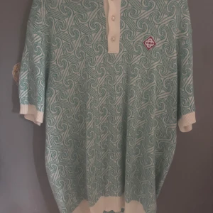 Casablanca mönstrad pikétröja - Säljer en unik pikétröja från Casablanca Tennis Club i ljusgrönt och vitt med swirl-mönster. Tröjan har korta ärmar, ribbade muddar och krage samt knappar framtill. Perfekt för dig som vill sticka ut med en cool och sportig vibe.