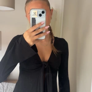 Svart långärmad knytblus Gina Tricot - Svart långärmad topp från Gina Tricot med snygg knytning framtill och djup v-ringning. Ärmarna är vida och materialet är mjukt och stretchigt, perfekt för en trendig look. Passar dig som gillar stilrena och enkla plagg med en twist. Skriv för mera bilder 💕