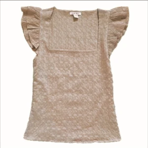 Beige blus med volangärmar från Amisu - Supersöt beige blus från Amisu med fyrkantig ringning och volangärmar. Toppen har ett subtilt strukturmönster i tyget och är lätt figursydd. Perfekt för dig som gillar en feminin och trendig look.