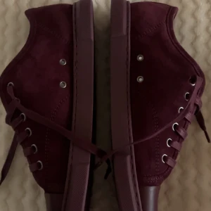 Vinröda sneakers från Lanvin - Snygga vinröda sneakers från Lanvin i mocka och skinn. Skorna har rund tå, platt sula och klassisk snörning. Skorna är sprillans nya från NK, men kan ej lämna tillbaka pga impregnering. Hör av er för mer info, kvitto mm🥰