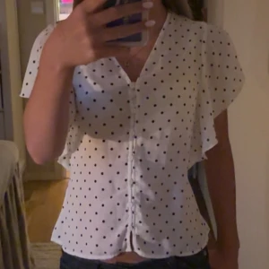 Vit prickig blus från Gina Tricot - Supersöt vit blus från Gina Tricot med svarta prickar, v-ringning och knappar hela vägen framtill. Blusen är helt ny men utan prislapp. Priset går att diskutera💕