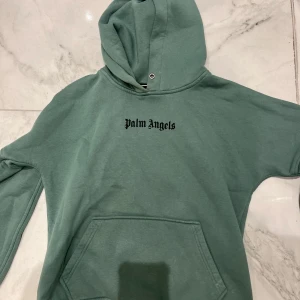 Grön Palm A hoodie med tryck - Snygg grön hoodie  med svart logotyptryck både fram och bak. Klassisk känguruficka och huva. Perfekt för dig som gillar streetwear och vill sticka ut med en trendig look. NOT REAL