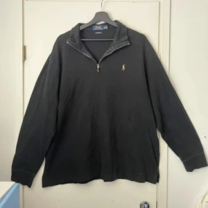 Svart half zip tröja Polo Ralph Lauren - Svart långärmad tröja från Polo Ralph Lauren med klassisk broderad logga på bröstet. Tröjan har en snygg half zip-dragkedja och är tillverkad i 100% bomull. Perfekt för en chill och stilren look.