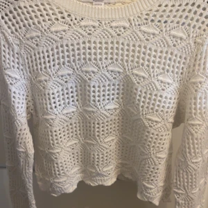 Vit stickad tröja med mönster - Superfin vit stickad tröja från Bershka med unikt hålmönster och långärmad modell. Tröjan har en rund halsringning och snygga detaljer i stickningen som ger en cool och luftig känsla. Perfekt att styla med jeans eller kjol för en trendig look.