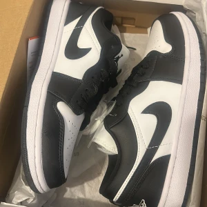 Nike Air Jordan 1 Low svart/vit - Snygga Nike Air Jordan 1 Low sneakers i svart och vitt skinn. Klassisk siluett med svart swoosh, snörning och vit mellansula. Perfekta för dig som vill ha en clean och tidlös look med streetkänsla. Låg modell som passar till det mesta.