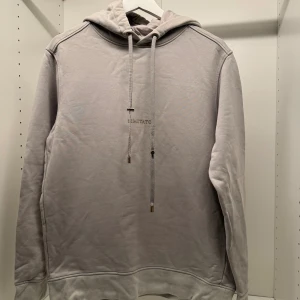 Ljusgrå hoodie från Limitato - Säljer en stilren ljusgrå hoodie från Limitato med broderad logga på bröstet. Tröjan har huva med snörning, långa ärmar och mjukt material som känns skönt mot huden. Perfekt för dig som gillar en clean och enkel look.