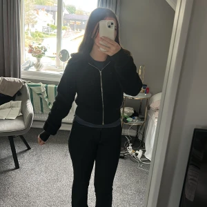 Svart fleece hoodie med dragkedja - Mysig svart hoodie i fleece med dragkedja framtill och huva. Tröjan är croppad och har långa ärmar, perfekt för kyliga dagar. Enkel och stilren design som passar till det mesta. Snygg och bekväm att slänga på sig när det är kallt ute.