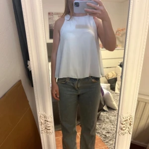 Vit ärmlös topp med öppen rygg från Zara - Säljer en vit, flowy ärmlös topp från Zara. Toppen har hög halsringning och en snygg öppen rygg med svart knytband. Perfekt för varma dagar och ger en cool, avslappnad vibe.