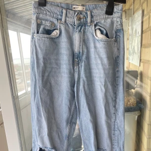 Ljusblå ripped jeans från Gina Tricot - Ljusblå jeans från Gina Tricot med stora slitningar över knäna. Klassisk femficksmodell i rak passform och normal midja. 