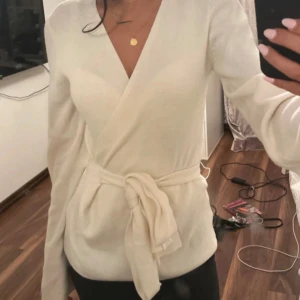 Vit omlottkofta med knytband - Säljer en superfin vit omlottkofta med knytband i midjan och v-ringad hals. Koftan har långa ärmar och är gjord i ett mjukt material som känns riktigt skönt mot huden. 