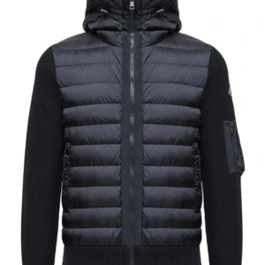 Svart Moncler pufferjacka med huva - Snygg svart pufferjacka från Moncler med stickade ärmar och vadderad framsida. Jackan har huva, dragkedja framtill och en praktisk ficka med dragkedja på ärmen. Perfekt för kyliga dagar och ger en sportig vibe.