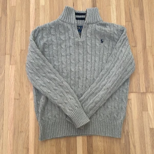 10-12 år grå tröja Ralph Lauren - Hejsan! Jag säljer min kabelstickade tröja från Ralph Lauren. Den säljs pga av att den är för liten på mig, men är i otroligt bra skick. Den finns nästan inget som tyder på användning och är i precis lika bra skick som att köpa en ny. Den är köpt på Åhléns city för 1.595,00 kr. Den har QR kod för att bekräfta att den är äkta.