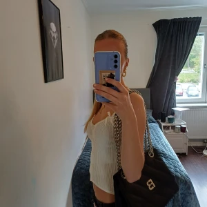 Svart handväska/sidoväska från NEY YORKER - Snygg svart axelväska med grov silverkedja som axelrem. Väskan har ett stilrent F-B-. Perfekt för dig som gillar en clean och modern look. Det får plats ganska mycket saker 