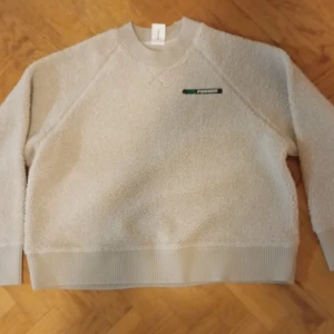 Beige fleece-tröja från Carin Wester - Mysig beige fleece-tröja från Carin Wester med ribbade muddar vid hals, ärmslut och nederkant. Tröjan har en enkel design med liten logga på bröstet och är perfekt för kyliga dagar. Oversized passform och långärmad modell.