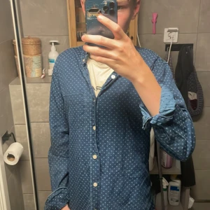 Blå prickig skjorta J.Lindeberg M - Snygg blå skjorta från J.Lindeberg i slim fit-modell med vita knappar och diskret prickigt mönster. Skjortan har lång ärm och klassisk krage, perfekt för dig som gillar stilrena detaljer och modern passform storlek s 