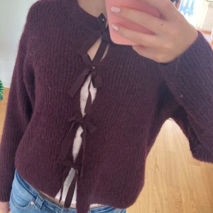 Vinröd kofta med rosetter från Gina Tricot - Superfin vinröd kofta från Gina Tricot i stickad ullmix. Koftan har långa ärmar och stängs framtill med flera dekorativa rosetter. Perfekt för höst och vinter när du vill vara både varm och snygg. Använd väldigt få gånger. Så mycket fint skick. 