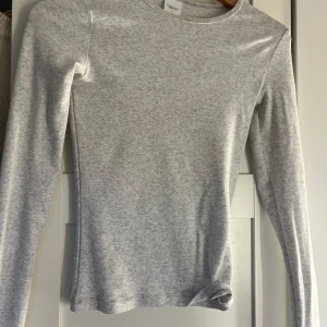 Helt ny Ljusgrå långärmad topp från Gina Tricot - En stilren ljusgrå långärmad topp från Gina Tricot, Elevated Basics. Slim passform med rund halsringning och mjukt bomullsmaterial. Perfekt att matcha med jeans eller kjol för en clean look. Ett impulsköp som jag ångrar hahah så säljer vidare. Haft på mig högst 1 gång inga defekter för utom kanske nån sminkfläck då jag köpt i affär