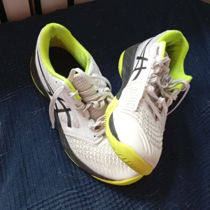 Innomhus skor - Säljer ett par Asics Netburner Ballistic FF sneakers/innomhus skor, i vitt med svarta detaljer och neongul insida och sula. Skorna har snörning, ventilerande mesh och en sportig design som passar perfekt för träning eller inomhussport. Sulan är slitstark och ger bra grepp. Jag änvänt dom i en säsong. Pris kan sänkas vid en villig affär