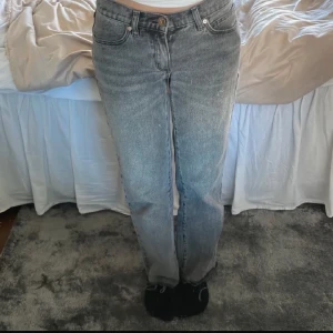 Grå raka jeans med vintagekänsla - Säljer ett par grå jeans med rak passform och klassisk femficksdesign. Jeansen har en snygg tvättad look som ger en vintagevibe. Materialet är robust denim och bakfickan har en liten läderpatch som detalj. 