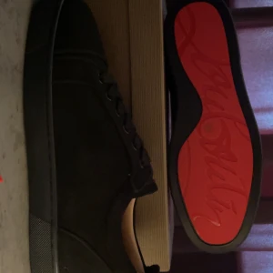 Svarta sneakers från Christian Louboutin - Exklusiva svarta sneakers från Christian Louboutin med signatur-röd sula och broderad logga på hälen. Skorna har snörning och är tillverkade i mocka med platt sula och rund tå. Kommer med originalförpackning, dustbag och äkthetsbevis.