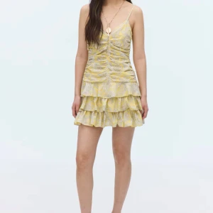 Gul volangklänning med smala axelband - Superfin kort gul klänning med smala axelband och flera volanger i kjolen. Klänningen har ett ljust blommigt mönster och rynkade detaljer framtill och baktill. Perfekt för sommarens alla tillfällen och ger en riktigt fräsch vibe. (Slutsåld)