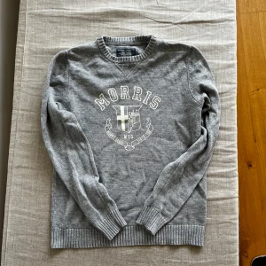 Morris tröja - Snygg grå tröja från Morris med broderad logga och emblem framtill. Väldigt fint skick. Tröjan är i storlek S men skulle även säga att den passar M. Hör av er vid fler bilder eller frågor!