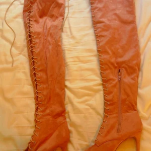 Bruna overknee stövletter med snörning - Säljer ett par bruna overknee stövletter med höga klackar. Skorna har snygg snörning längs hela framsidan och dragkedja på insidan för enkel påtagning. Tillverkade i mocka-look som ger en lyxig känsla. Perfekta för dig som vill sticka ut.