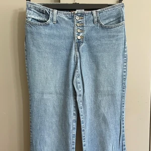  jeans wide fit Bendetta 29 - Ljusblå jeans med knappgylf och raka, vida ben. Jeansen har fem fickor, bälteshällor . Tillverkade i denim av bomull, perfekt för en avslappnad och trendig look. Midjemått 79/80 cm , längd 102 cm