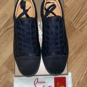 Christian Louboutin svarta sneakers mocka - Snygga svarta sneakers från Christian Louboutin i mocka med klassisk röd sula. Skorna har rund tå, svarta snören och diskreta detaljer. Perfekta för dig som vill ha en lyxig och stilren look med en ikonisk touch.