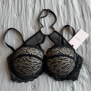 Oanvänd Svart spetsig bh från Caprice - Snygg svart korsett-topp från Caprice med spetsdetaljer och meshpartier. Toppen har justerbara axelband, vadderade kupor och dekorativa kanter. Man kan ta av axelbanden helt. Skulle säga den är en storlek mindre i kupa🫶🏻