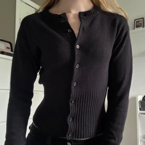 Svart kofta - Svart stickad kofta från NELLY med rund halsringning och knappar hela vägen framtill. Tröjan har långa ärmar och en bred ribbad midja och ärmslut som ger en snygg, figurnära passform💗