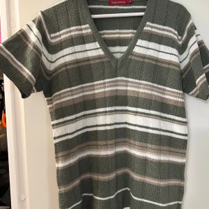 Randig stickad tröja Think Positive strl: XL - Randig stickad tröja från Think Positive i grönt, beige och vitt. Modellen har v-ringning, korta ärmar och ribbad struktur. Perfekt för dig som gillar en avslappnad men ändå snygg stil. Förekommer noppor. Material: 100% acrylic.