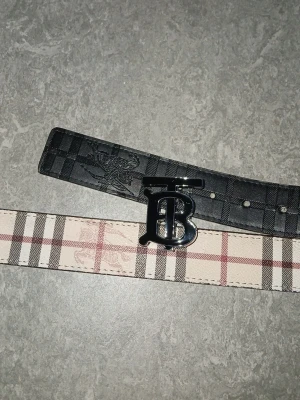 Burberry bälte 2 sidig - Snyggt Burberry bälte med det ikoniska rutmönstret i beige och svart. Bältet har en stor metallspänne med Burberrys logga framtill. Tillverkat i läder med exklusiv känsla och passar perfekt för att lyfta din outfit. UTAN BOX!