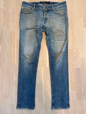 Limited edition Jacob Cohen med slitningar|133/156 - Snygga blå jeans från Jacob Cohen med slitna detaljer. Jeansen har klassisk femficksmodell, knäppning med knappar och coola insydda detaljer i midjan. Perfekta för en avslappnad och trendig look. Jeansen är limited edition och är nummer 133 av 156. Detta är alltså ett par sällsynta jeans så passa på!