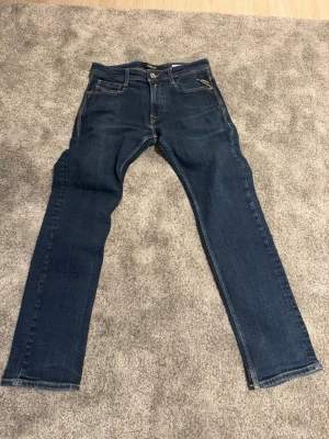Replay Rocco blå jeans - Snygga blå jeans från Replay, modell Rocco. Klassisk femficksdesign med Replay-logga på myntfickan. Jeansen har raka ben och kontrastsömmar för en stilren look. Perfekta till vardagsoutfiten och tillverkade i mjukt denimtyg. Finns en liten fläck som knappt syns och ses i bild 7, går nog bort ganska lätt! W28 L30 skriv för frågor och skicka gärna bud!