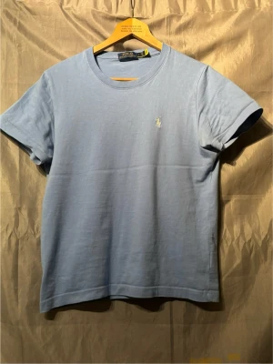 Ljusblå t-shirt från Polo Ralph Lauren - Snygg ljusblå t-shirt från Polo Ralph Lauren med klassisk passform och liten broderad logga på bröstet. Tillverkad i mjuk bomull och har rund halsringning samt korta ärmar. Perfekt basplagg för en clean och stilren look. 100% bomull