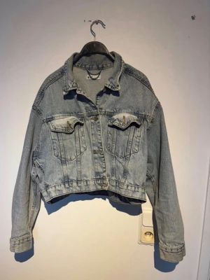 Cropped jeansjacka från Gina Tricot - Snygg ljusblå cropped jeansjacka från Gina Tricot med klassisk krage, två bröstfickor med lock och knapp samt knappstängning framtill. Obs vet ej fall fläckarna vid kragen går bort i tvätten , kort i modellen