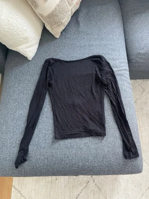 Svart långärmad topp med öppen rygg - Trendig svart långärmad topp med en snyggt öppen rygg. Modellen är tight, perfekt att styla med höga jeans eller kjol. Tillverkad i mjukt stretchigt material för en bekväm passform. Enkel men ändå statement med sin djupa ryggskärning.