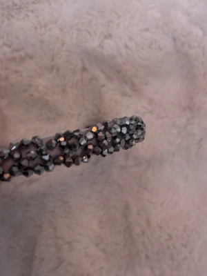 Diadem med svarta och silvriga stenar - Snyggt diadem täckt med glittrande svarta och silvriga stenar som ger en riktigt cool och trendig look. Diademet har en klassisk bågform och är perfekt för att lyfta vilken outfit som helst. Materialet är troligtvis plast med dekorerade stenar för extra bling.