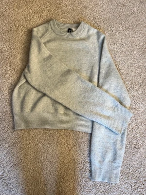 Ljusgrå stickad tröja från H&M Divided - En stilren ljusgrå stickad tröja från H&M Divided. Tröjan har rund halsringning, långa ärmar och ribbade muddar vid ärmslut och nederkant. Perfekt för lager på lager och enkel att matcha med jeans eller kjol.