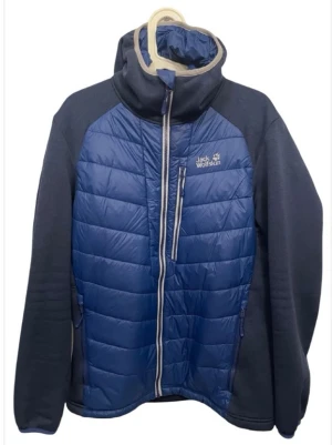 Blå pufferjacka från Jack Wolfskin - Säljer en blå pufferjacka från Jack Wolfskin med Stormlock och Microguard Maxloft QMC-teknologi. Jackan har hel dragkedja, hög krage och två sidofickor med dragkedja. Materialet är polyester och fleece, perfekt för kyliga dagar.