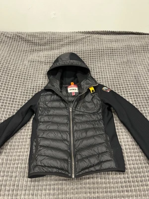 Svart dunjacka från Parajumpers - Snygg svart dunjacka från Parajumpers med huva och dragkedja framtill. Jackan har quiltad framsida, släta ärmar och en gul detalj vid kragen. Perfekt för kalla dagar och har en sportig look. Nypris 3500kr haft i 8 månader inte använd så mycket, OBS Den är inte till vuxna har ni frågor kontakta mig innan
