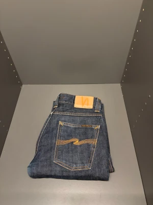  Nudie Jeans slim Jim  - Snygga mörkblå jeans från Nudie Jeans med klassisk femficksdesign och kontrastsömmar. Jeansen har en rak passform och är tillverkade i slitstark bomullsdenim. Perfekta för dig som gillar stilrena och tidlösa jeans. W30 L32